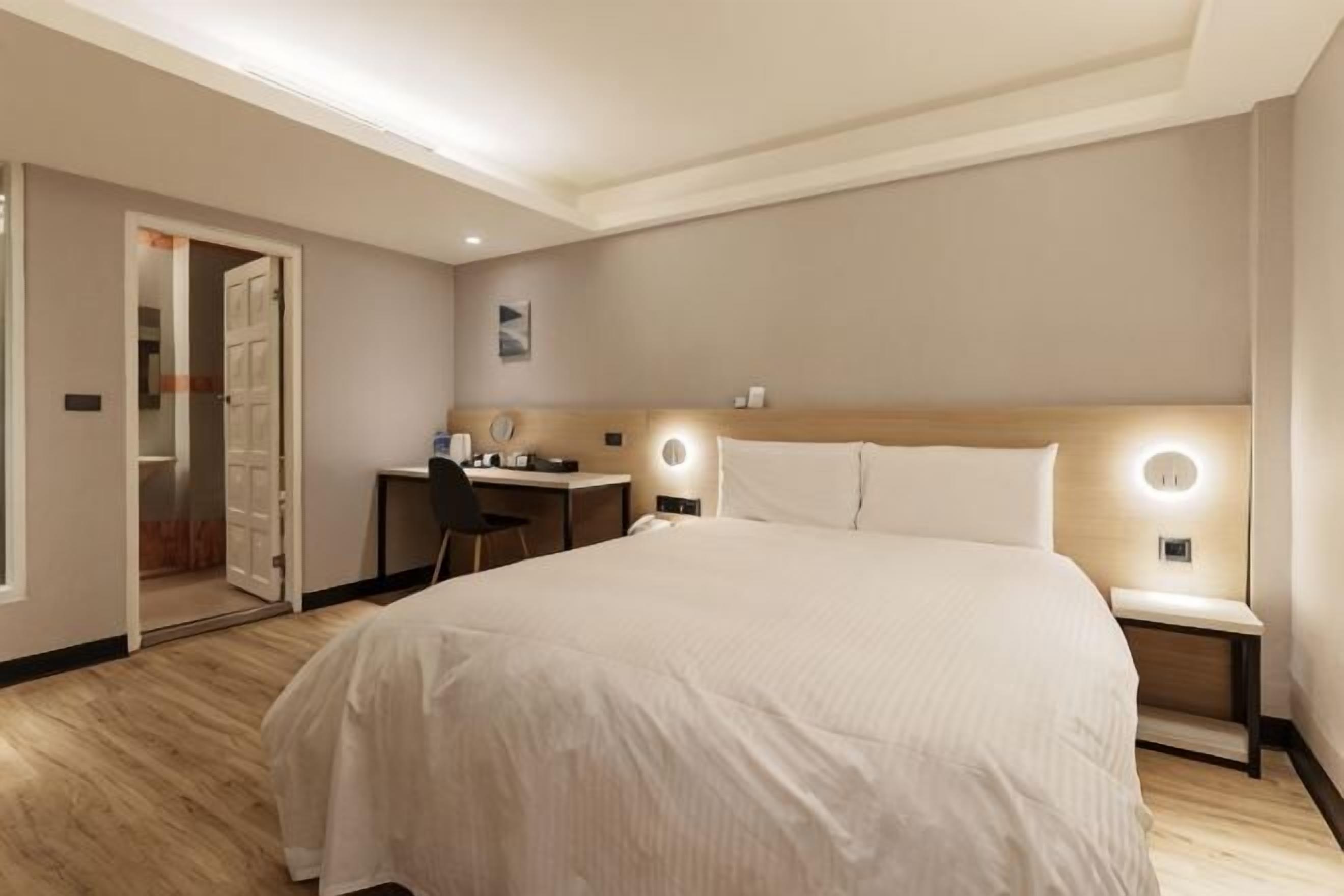 Quarto de hotel com cama, escrivaninha e abajures.