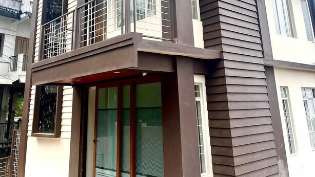 Une maison moderne à deux étages, dotée d’un balcon, de grandes fenêtres et d’un toit plat.