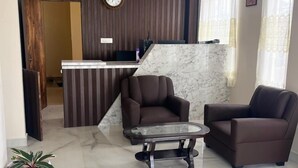 Un hall d’entrée moderne avec un sol en marbre, deux fauteuils en cuir, une table basse en verre, un comptoir d’accueil et une horloge murale.