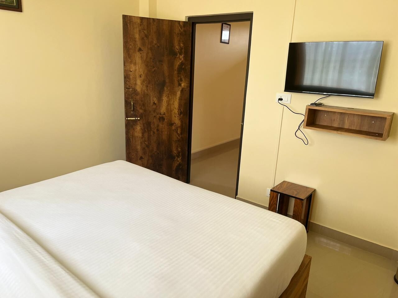 Une chambre à coucher comprenant un lit, une armoire, un téléviseur et une petite table d’appoint en bois.