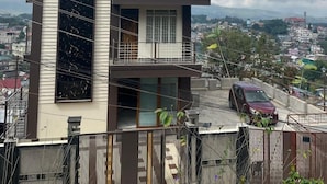 Il s’agit d’un immeuble à deux étages, sur lequel on peut lire l’inscription « Grace Guest House ». Il possède un balcon à l’étage supérieur et une grande fenêtre au rez-de-chaussée.