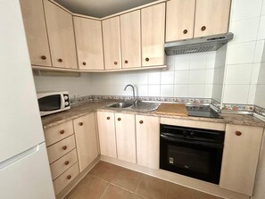 A compact kitchen with light wooden cabinets, a microwave, a sink, a dishwasher, and a stove. - Apartment with large terrace and sea view (Torremolinos)