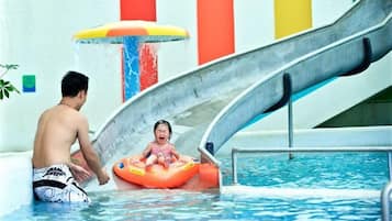 A pool with a water slide, a child on an inflatable tube, and a man in swim trunks.