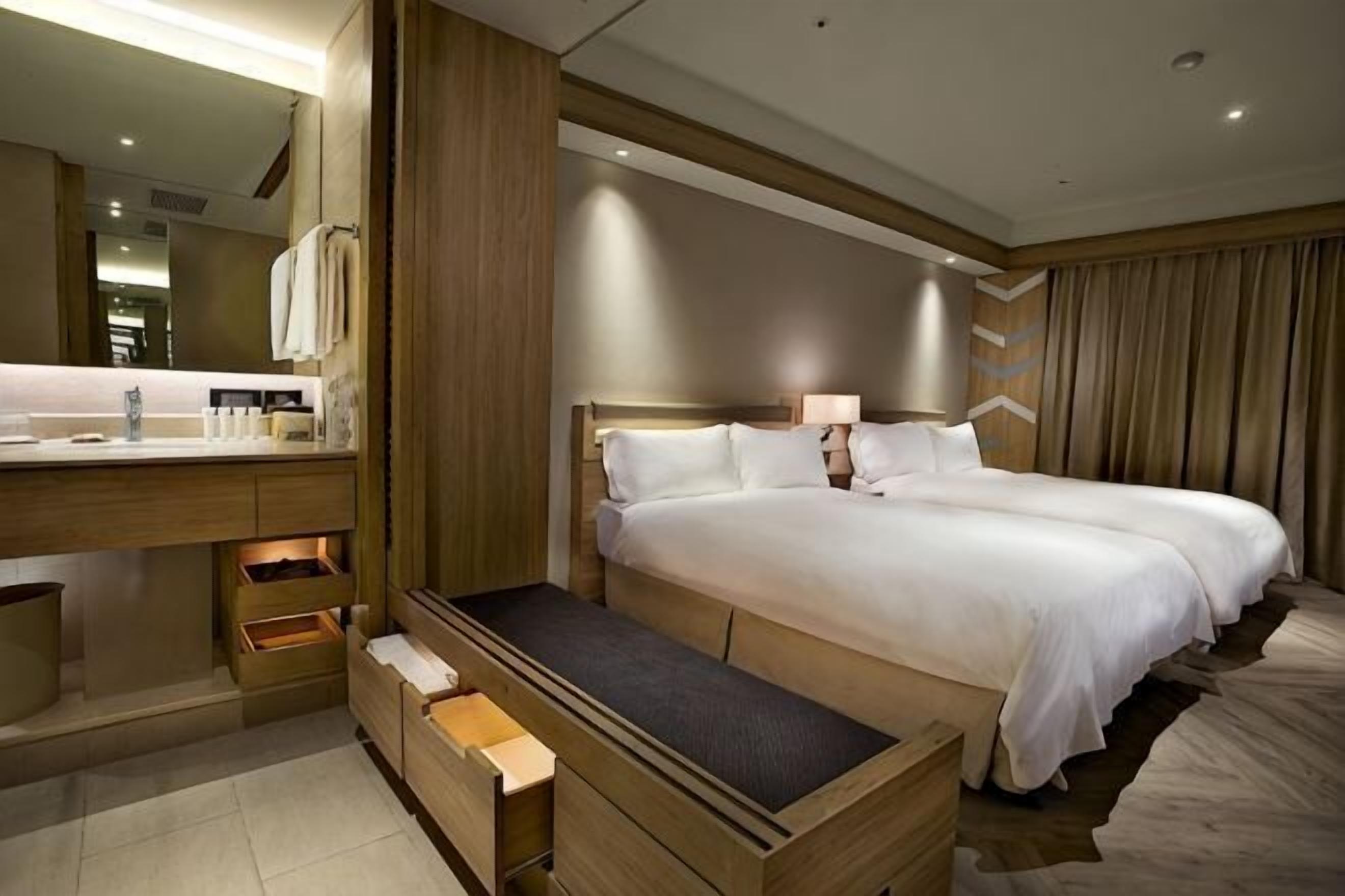 Une chambre d’hôtel avec un grand lit, une coiffeuse en bois, un miroir et une table de chevet.