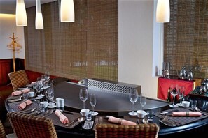 A dining area with a round table set for a meal, surrounded by chairs, and a view through a window with blinds. - Hotel Royal Chihpen Spa (Taitung)