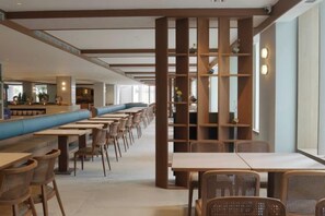 Een restaurant met lange gedeelde tafels en zitbanken, een barhoek en een uitzicht door een houten scheiding.