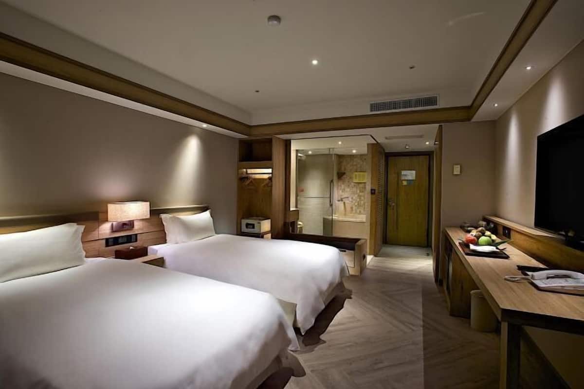Ein Hotelzimmer mit zwei Betten, einem Schreibtisch, einem Fernseher und einem durchgegangenen Tür sichtbaren Badezimmer.