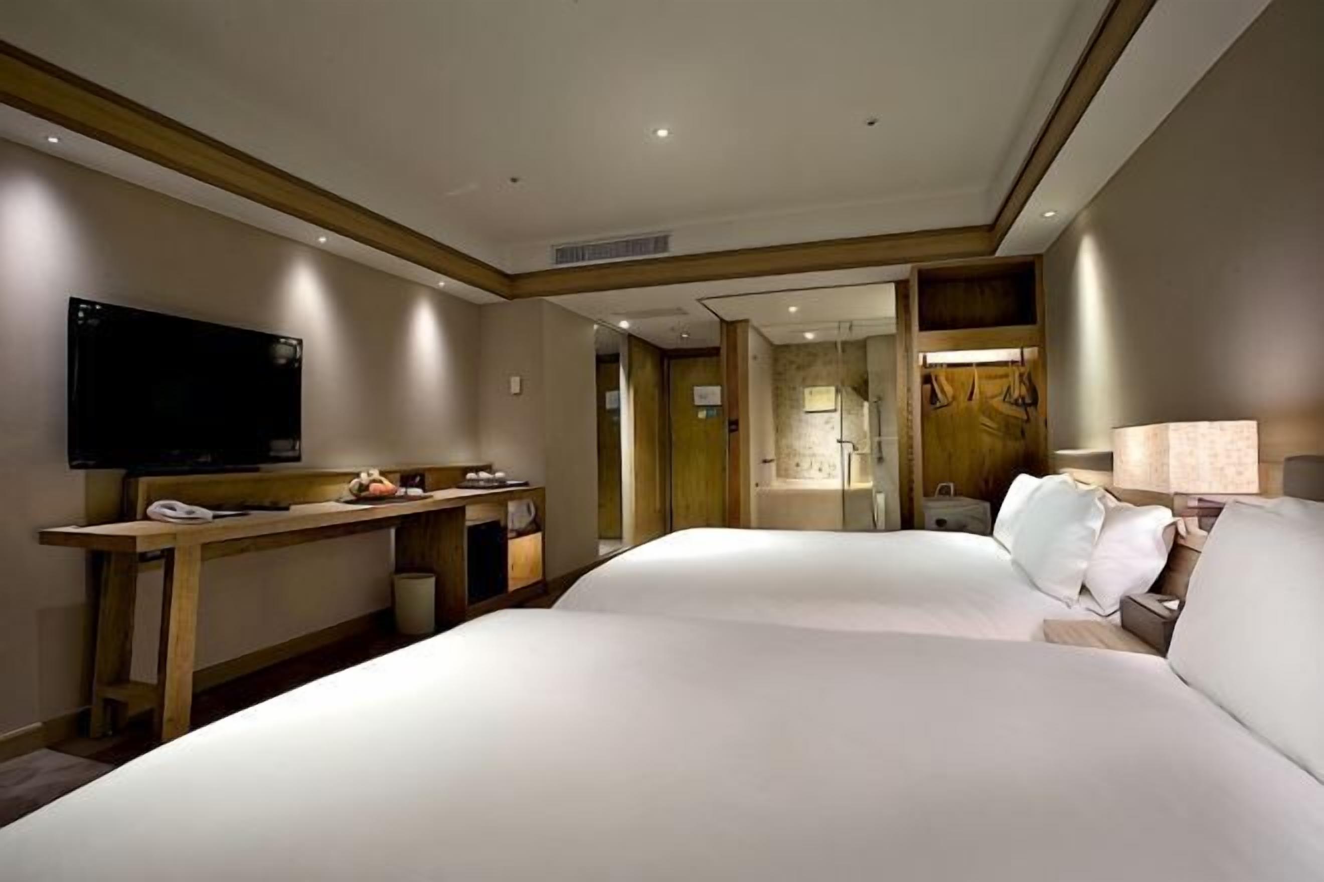 A hotel room with two beds, a TV, a desk, and a lamp.