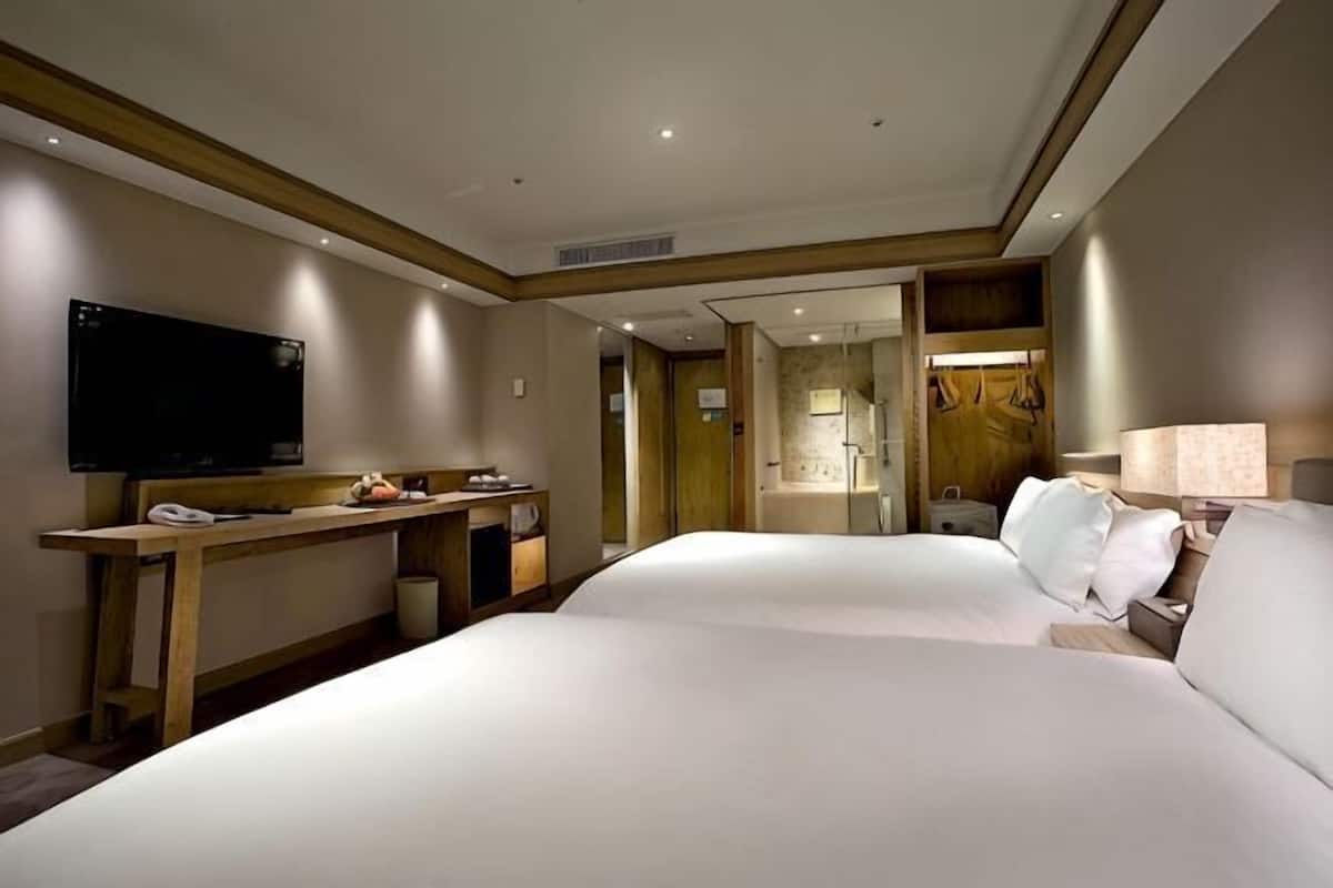 Ein Hotelzimmer mit zwei Betten, einem Fernseher, einem Schreibtisch und einer Lampe.