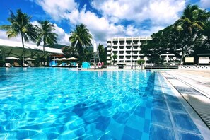 A swimming pool with clear blue water, surrounded by palm trees and a hotel building in the background. - Hotel Royal Chihpen Spa (Taitung)