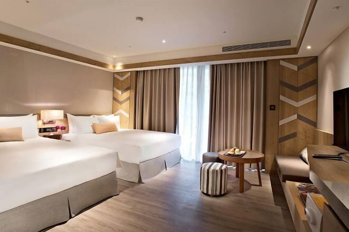 Ein Hotelzimmer mit zwei Betten, einem kleinen runden Tisch mit Obstschale, einer Couch und einem Fernseher.