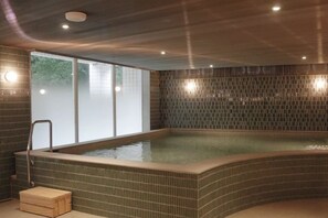 A spa with a large, curved hot tub, a wooden bench, and a glass wall with a view of trees. - Hotel Royal Chihpen Spa (Taitung)