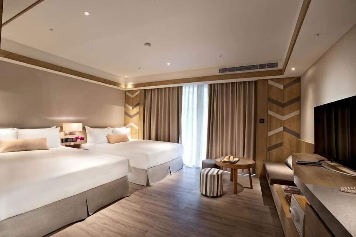 Ein Hotelzimmer mit zwei Betten, einem Schreibtisch, einem Fernseher und einem fenster mit Vorhängen.