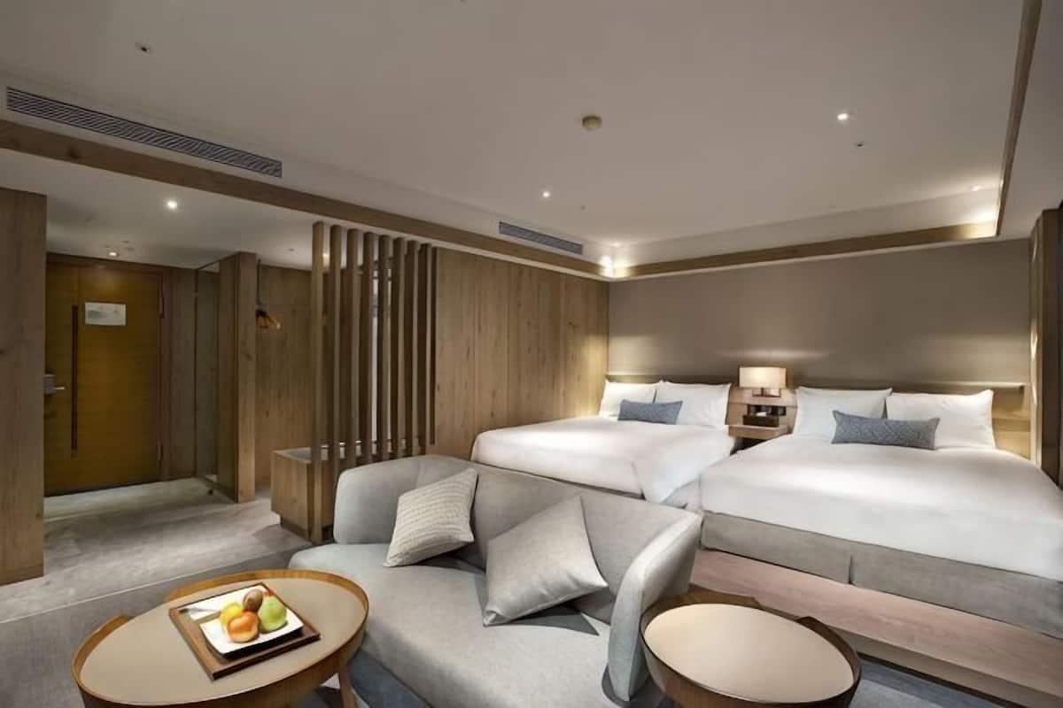 Ein Hotelzimmer mit einem Doppelbett, einem Schlafsofa, einem kleinen Tisch mit Obst und einer dekorativen Wandverkleidung.