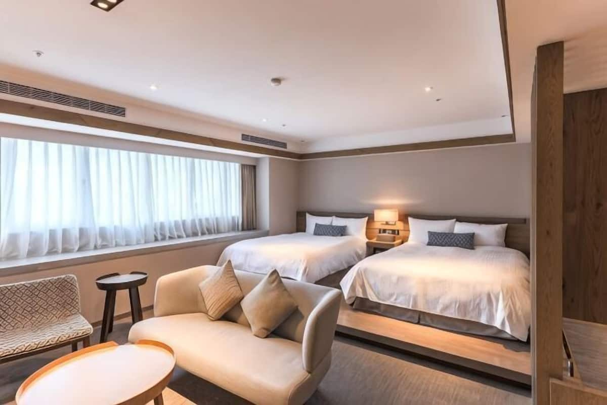 Ein Hotelzimmer mit zwei Betten, einem Sofa, einem kleinen Tisch und einem Fenster mit Vorhängen.