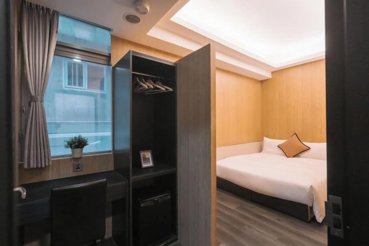 Une chambre d’hôtel moderne équipée d’un lit, d’une armoire, d’un bureau et d’une fenêtre avec des rideaux.