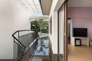 Un interior moderno con balaustrada de vidrio, televisor de pantalla plana y vistas al exterior con vegetación.