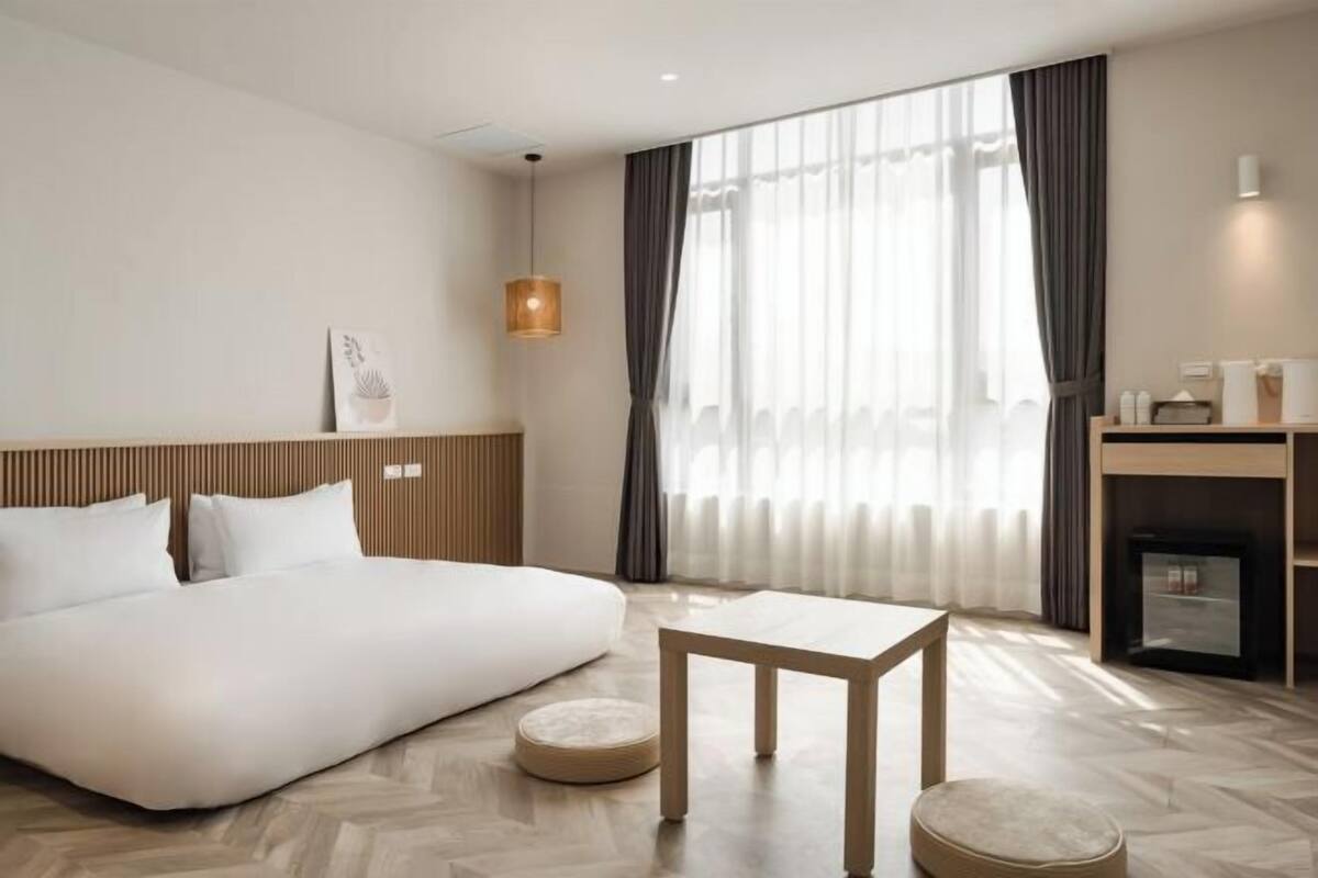 Habitación de hotel con cama, una mesita, un otoman redonda, chimenea y un ventanal con cortinas.