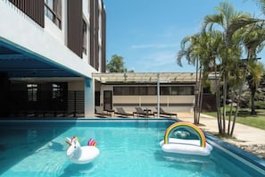 A swimming pool with two inflatable swan floats and a rainbow float, surrounded by lounge chairs and palm trees. - Shan Ban Bay By Riverinn (Pingtung)