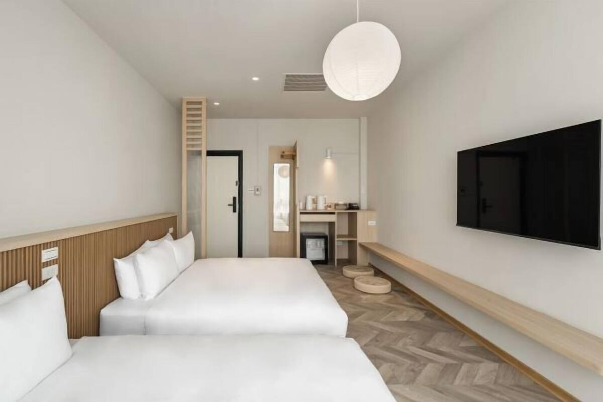 Habitación de hotel con dos camas, televisión, escritorio con silla y suelo de madera.