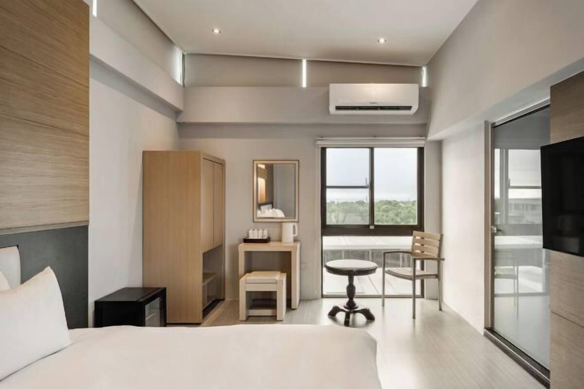 Habitación de hotel moderna con cama, escritorio con silla, una mesita, armario y un ventanal con vistas.