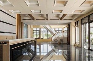 Un vestíbulo espacioso con un piso de mármol pulido, una escalera y grandes ventanales que dejan entrar luz natural.