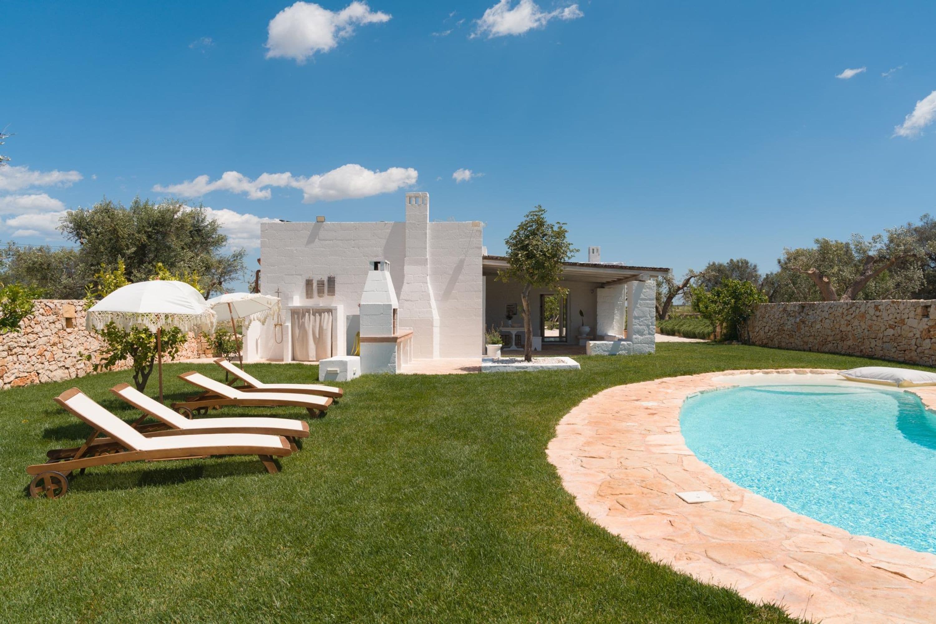 Una villa moderna con piscina, mobiliario exterior y un muro de piedra.
