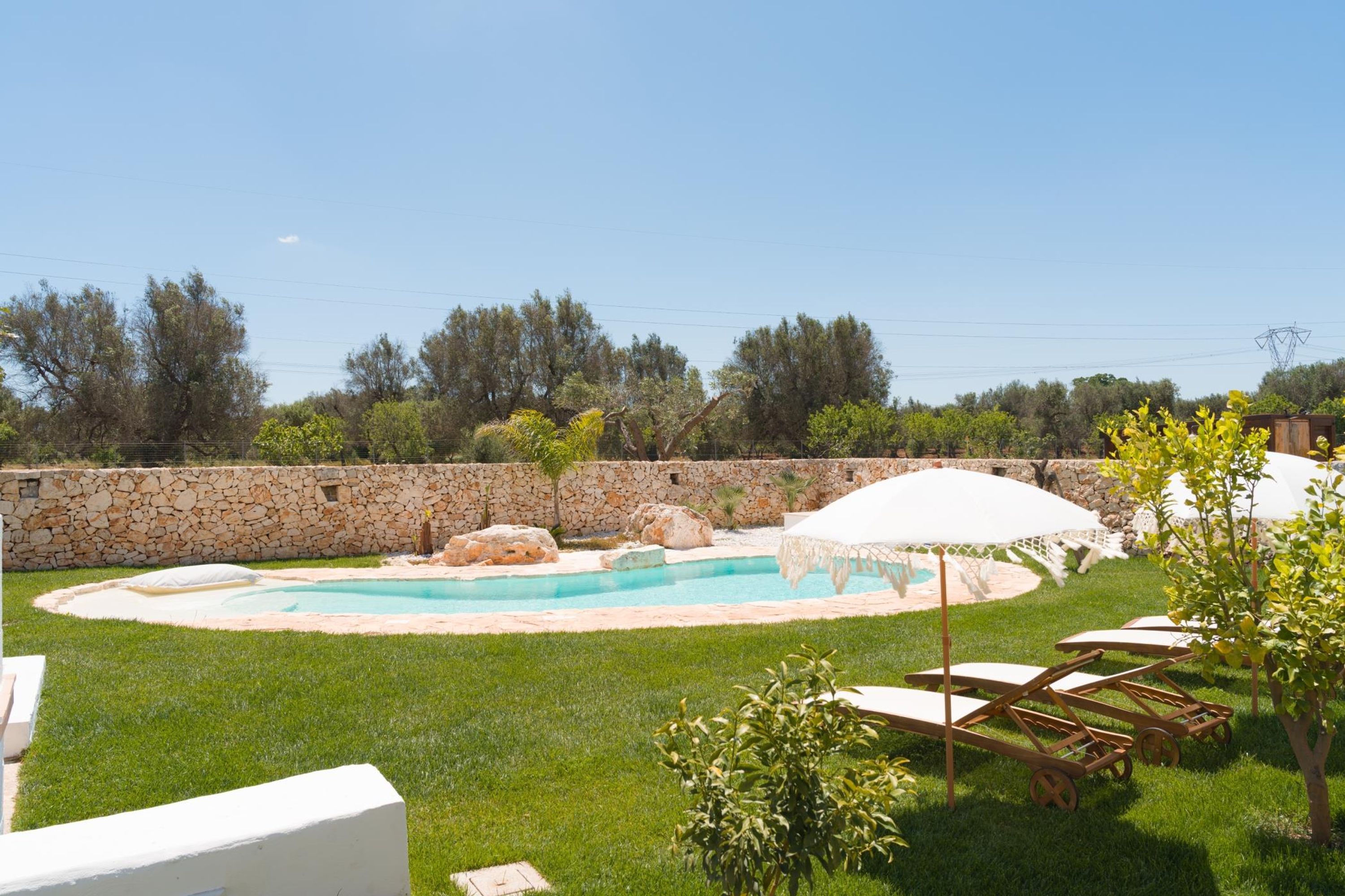 A backyard with a swimming pool, stone wall, and lounge chairs.