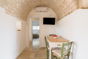 A narrow hallway with a tiled floor, a wooden table with chairs, a mounted TV, and a stone wall. - Villa Gia con Piscina Privata (San Michele Salentino)