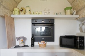 A kitchen with a built-in oven, a microwave, and a shelf with various kitchenware. - Villa Gia con Piscina Privata (San Michele Salentino)