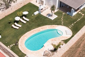 A swimming pool with a stone border, surrounded by a lawn with lounge chairs and umbrellas. - Villa Gia con Piscina Privata (San Michele Salentino)