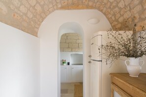 A kitchen with white cabinets, a stone wall, and a door leading to another room. - Villa Gia con Piscina Privata (San Michele Salentino)