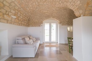 A room with a stone ceiling, a white sofa, a dining table with chairs, and a large arched doorway. - Villa Gia con Piscina Privata (San Michele Salentino)