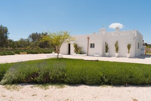 A white building with a flat roof, a door, and a small window. There is a tree in front of the building and a gravel driveway. - Villa Gia con Piscina Privata (San Michele Salentino)