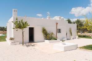 A white building with a door, windows, and a small garden area with potted plants. - Villa Gia con Piscina Privata (San Michele Salentino)