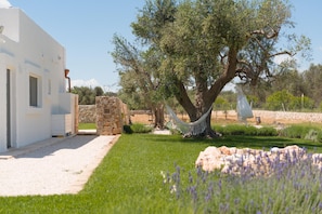 A white building with a stone wall, a large tree, and a hammock. - Villa Gia con Piscina Privata (San Michele Salentino)