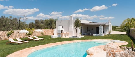 Une maison moderne dotée d’une piscine, d’un espace salon extérieur et d’un mur en pierre.