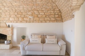 A cozy living room with a stone wall, a fireplace, and a beige sofa with 'relax.' pillows. - Villa Gia con Piscina Privata (San Michele Salentino)