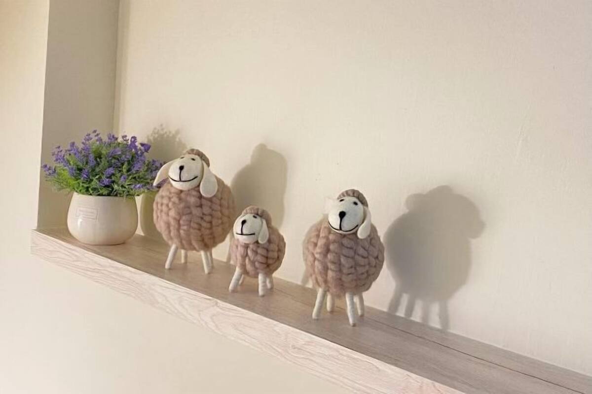 Una estantería con tres figuritas de ovejas y una maceta con flores moradas.