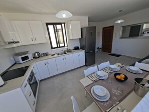 Eine moderne Küche mit weißen Schränken, einem Edelstahl-Kühlschrank und einem Essbereich für vier Personen, ausgestattet mit Tisch, Stühlen und einer Obstschale.