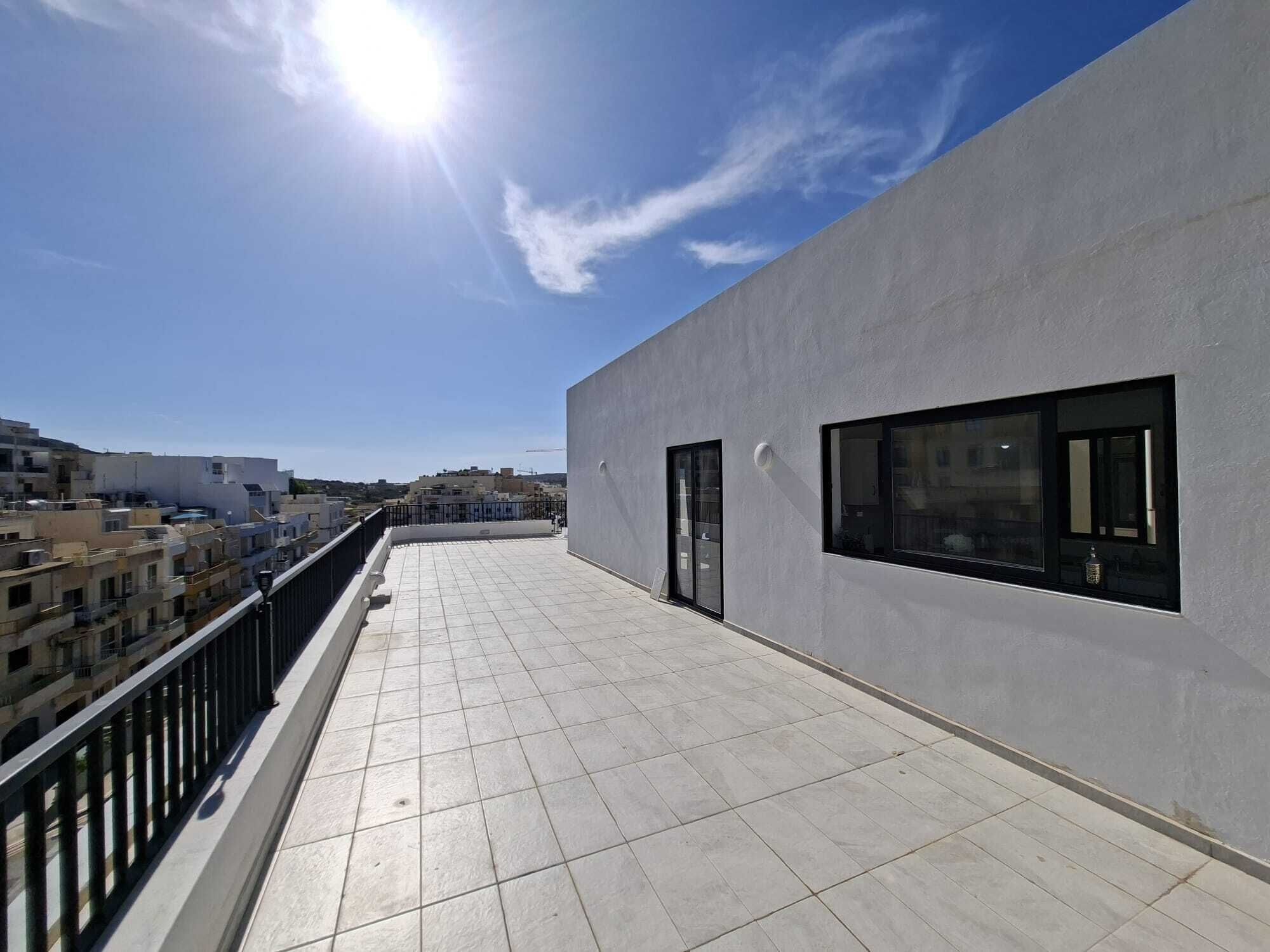 A rooftop terrace with a clear view of the cityscape, featuring a modern building with large windows and a tiled floor.