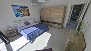 Un dormitorio con cama, armario, mesita de noche, silla y un jarrón con flores.