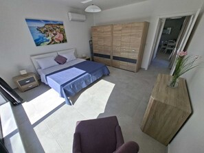 Ein Schlafzimmer mit einem Bett, einem Kleiderschrank, einem Nachttisch, einem Sessel und einer Vase mit Blumen.