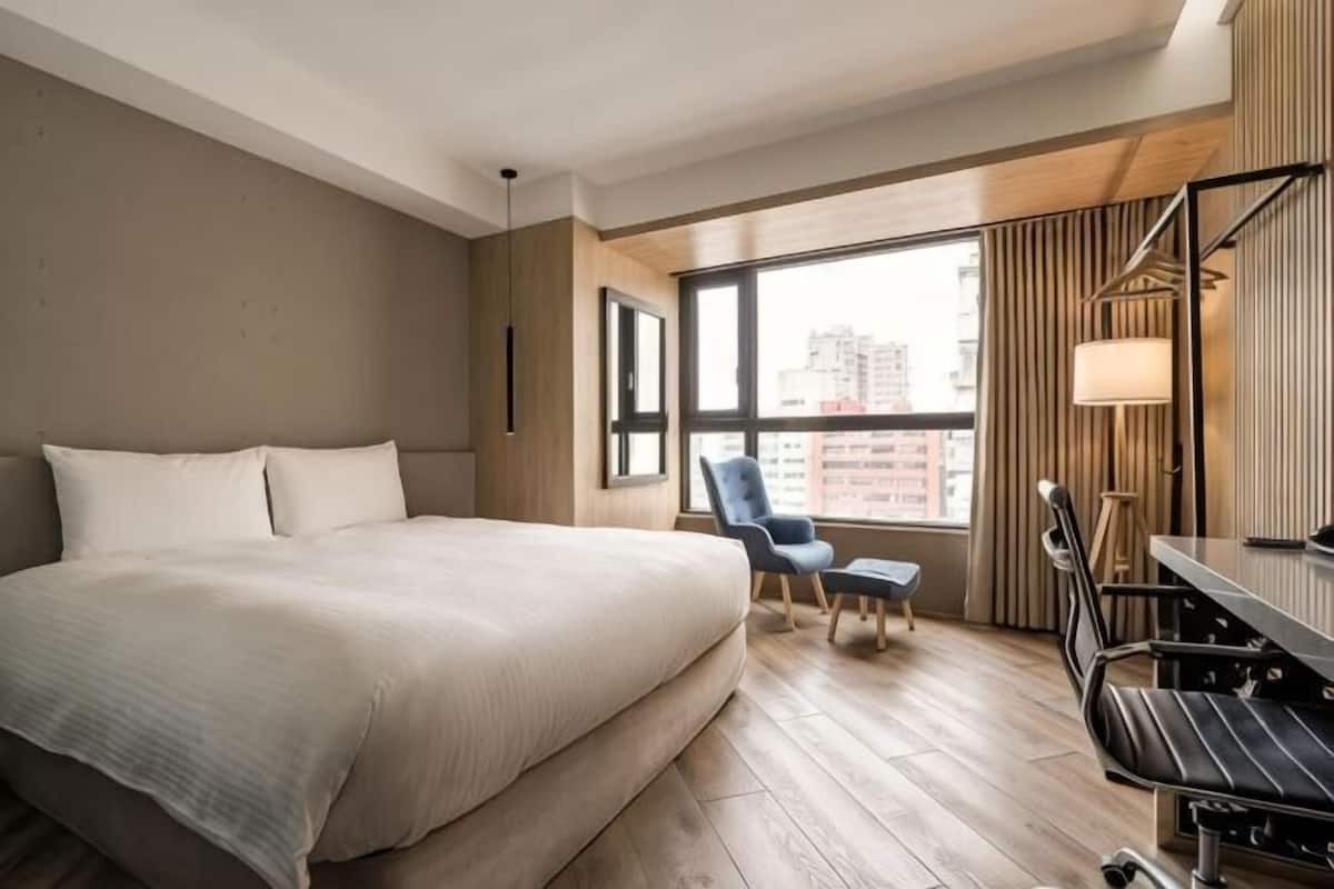 Habitación de hotel con una cama grande, un escritorio, una silla y una ventana con vistas a la ciudad.