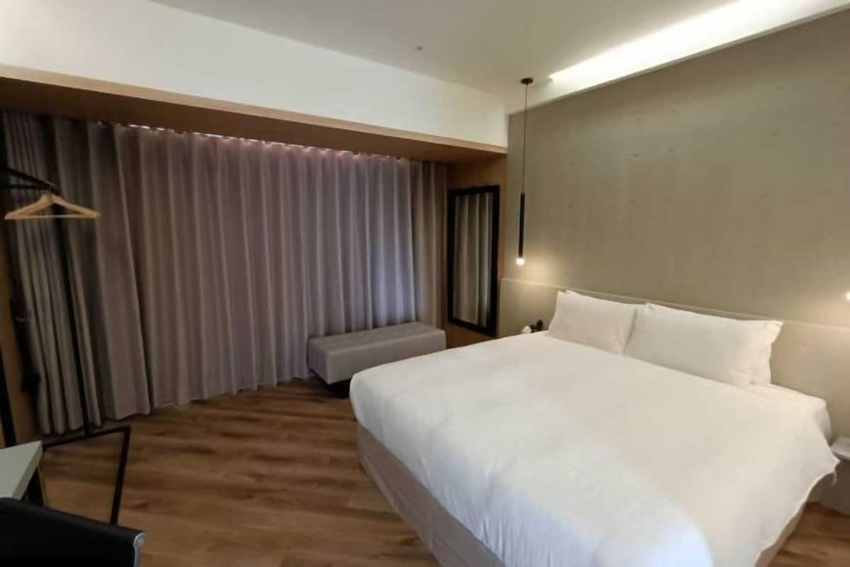 Una habitación de hotel moderna con una cama grande, suelo de madera, un banco y un perchero.