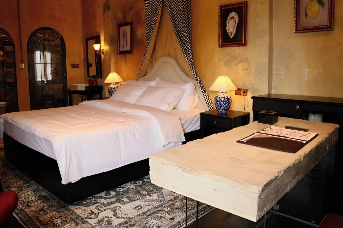 A hotel room with a large bed, a bedside table with a lamp, a small table with a menu, and a decorative wall piece.