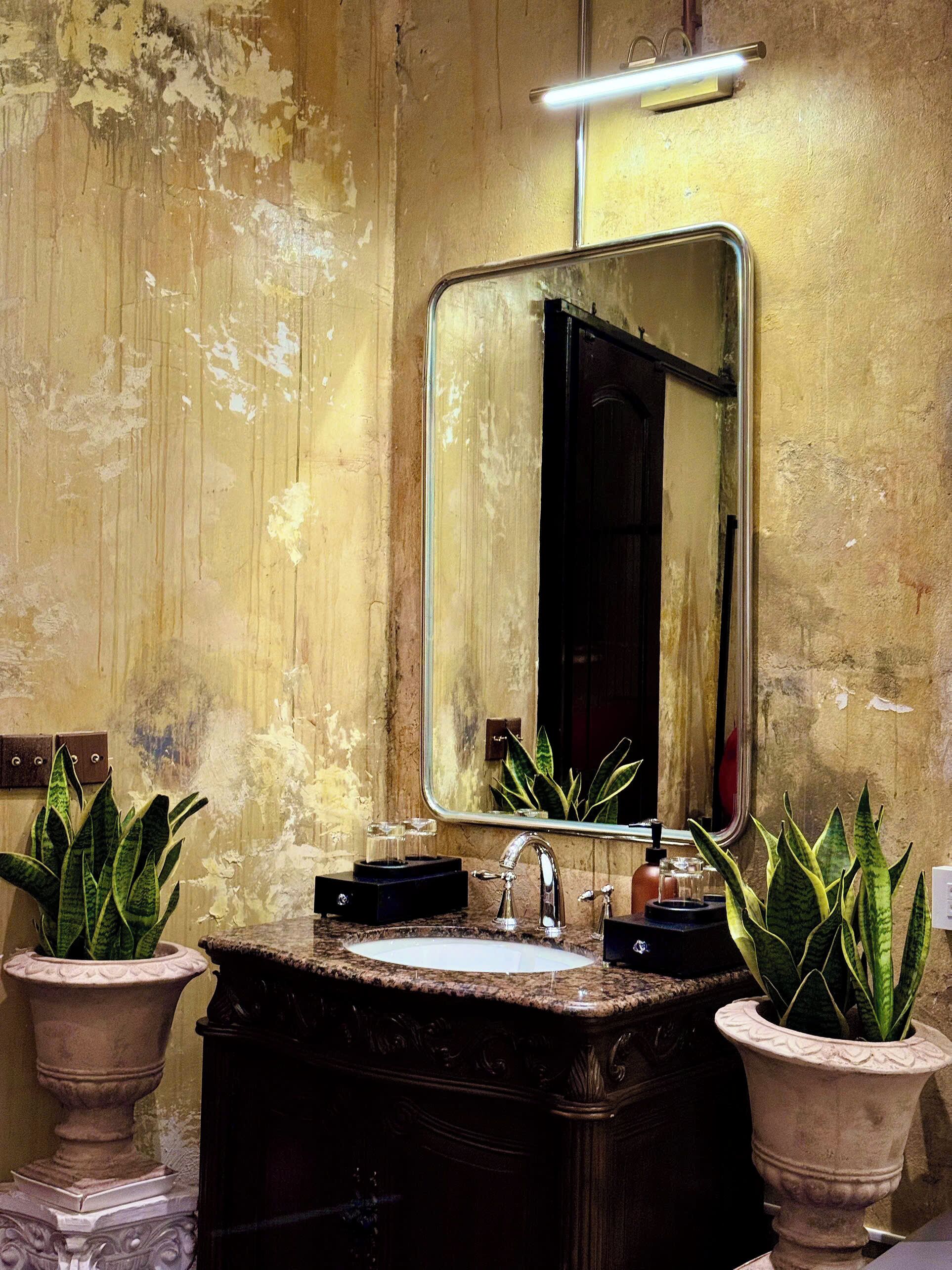 A bathroom with a sink, mirror, and two potted plants.