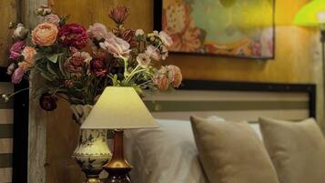A room with a bed, a small table with a lamp, and a painting on the wall.