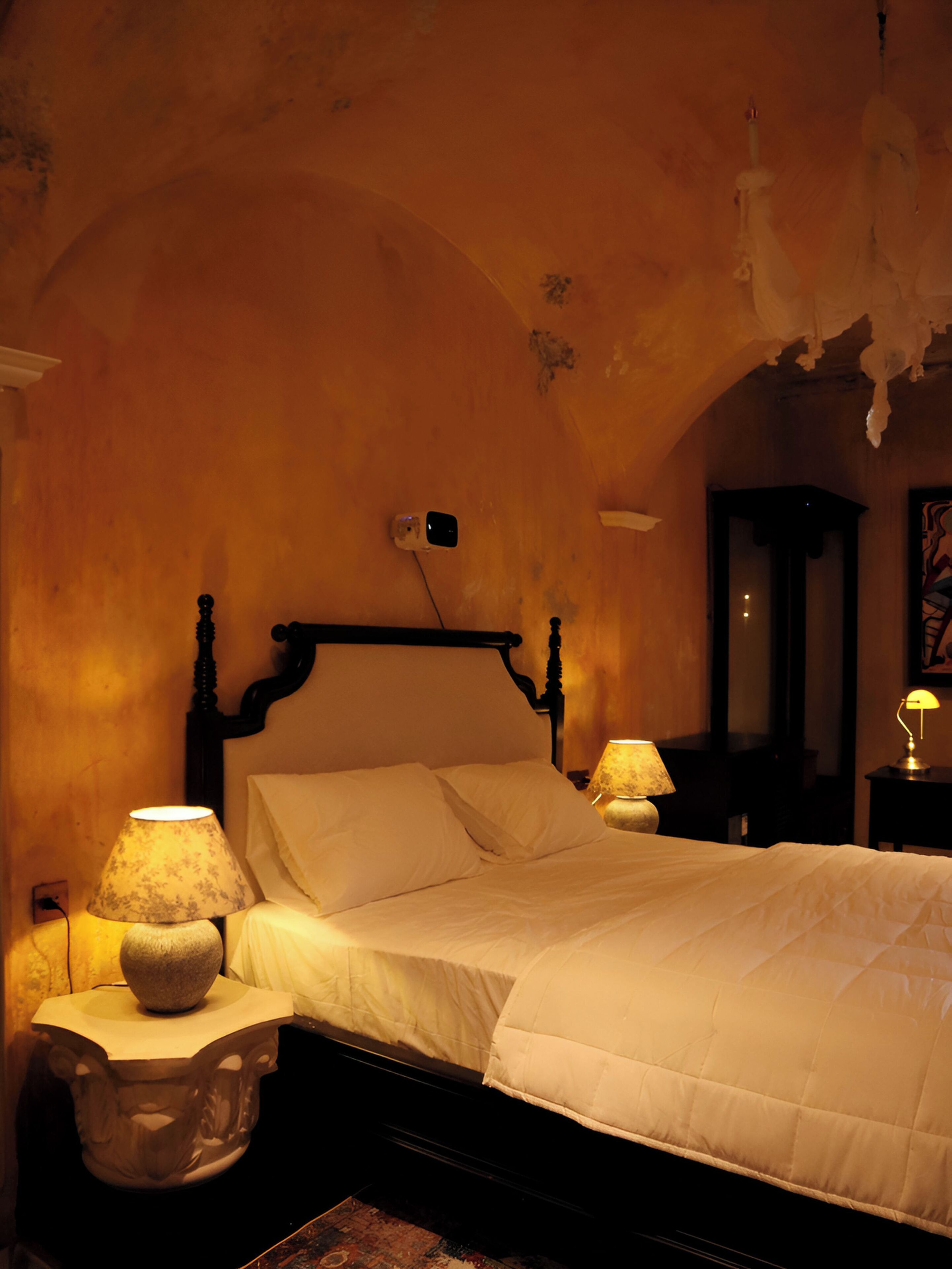 A bedroom with a bed, two bedside tables with lamps, a mirror, and a chandelier.