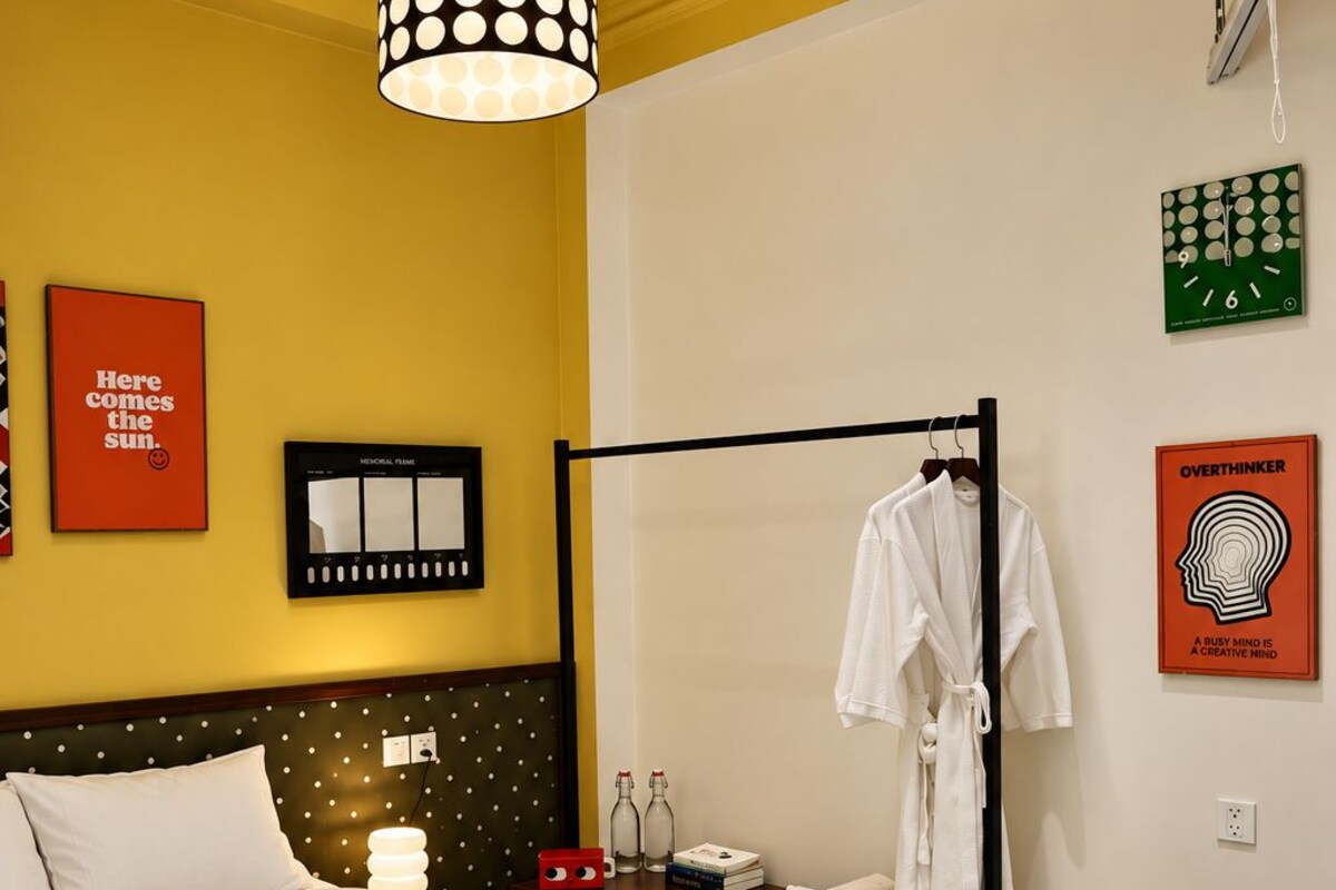 Habitación de hotel con cama, mesita de noche, perchero, un reloj en la pared y una alfombra verde estampada.